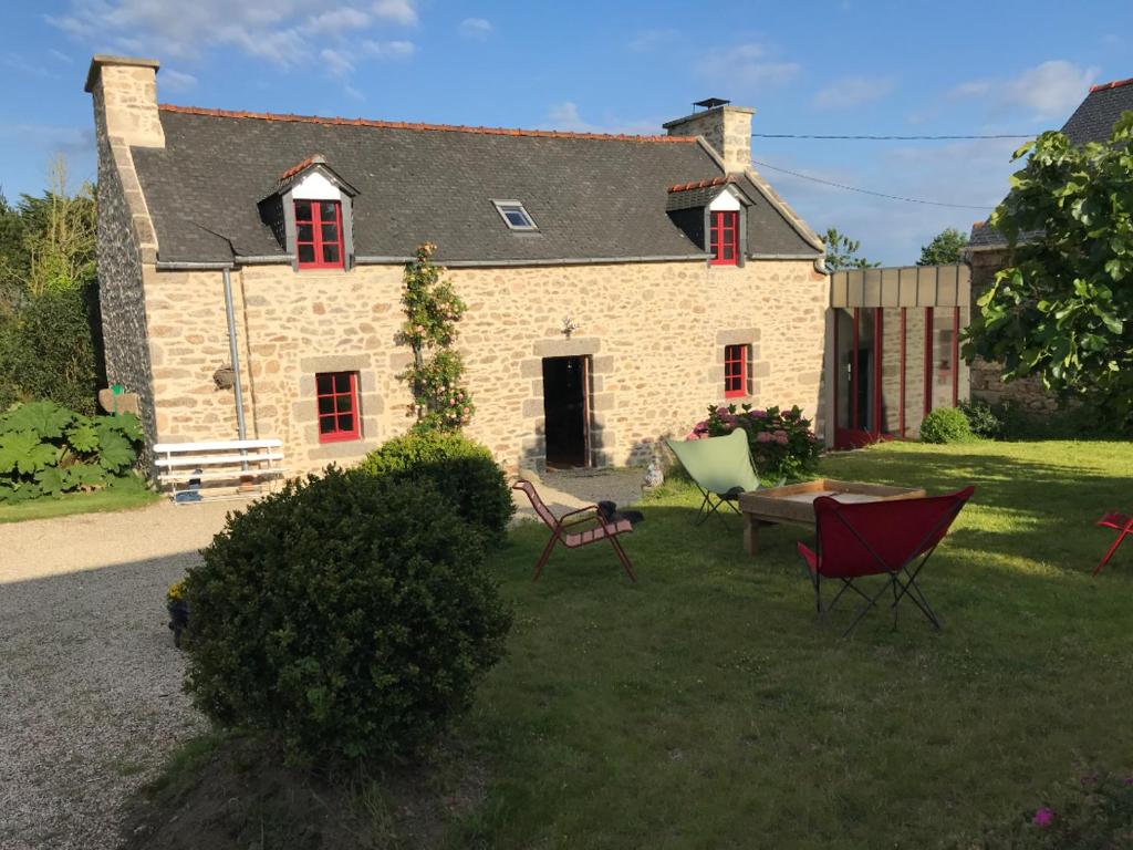 une maison en pierre avec des fenêtres rouges, une table et des chaises dans l'établissement LocMajan, à Plouguin
