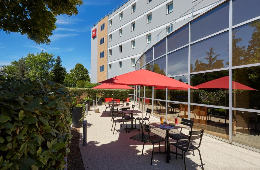 une rangée de tables avec des parasols rouges devant un bâtiment dans l'établissement ibis Archamps Porte de Genève, à Archamps