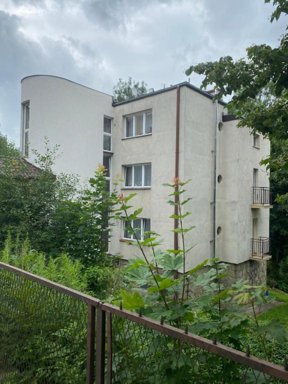 Biały budynek z płotem przed nim w obiekcie Apartament nad Kryniczanką w mieście Krynica Zdrój
