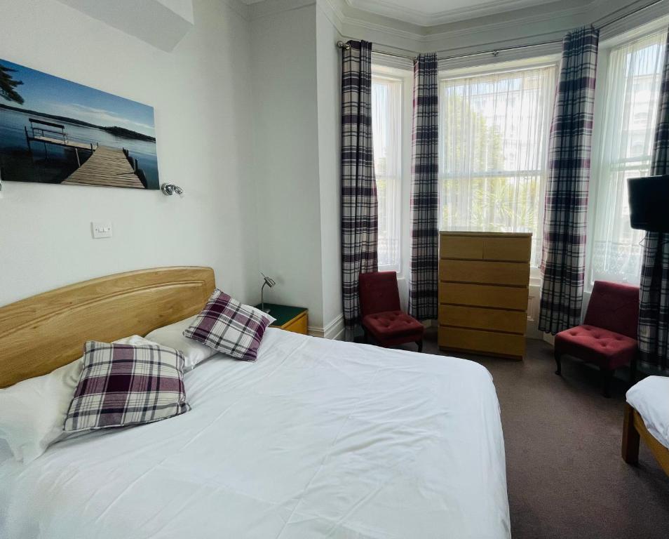 a bedroom with a bed and two chairs and windows at Devonshire House Holiday Flats in Eastbourne