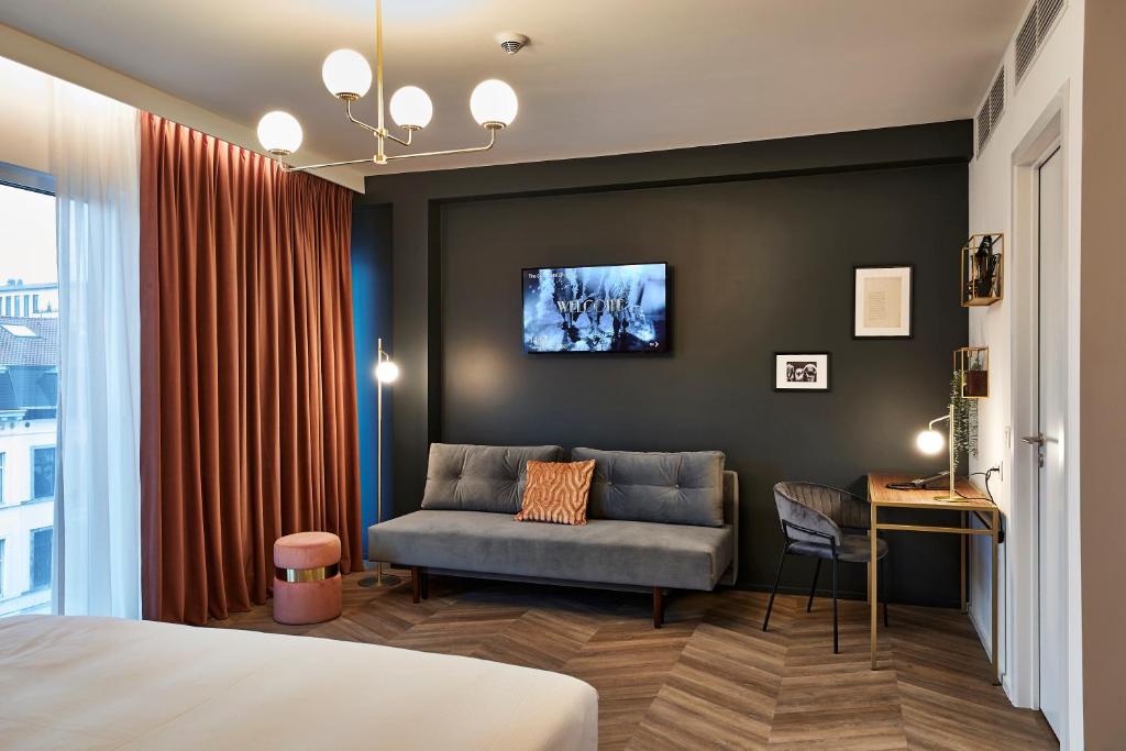een slaapkamer met een bank en een tv aan de muur bij The Scott Hotel Brussels in Brussel