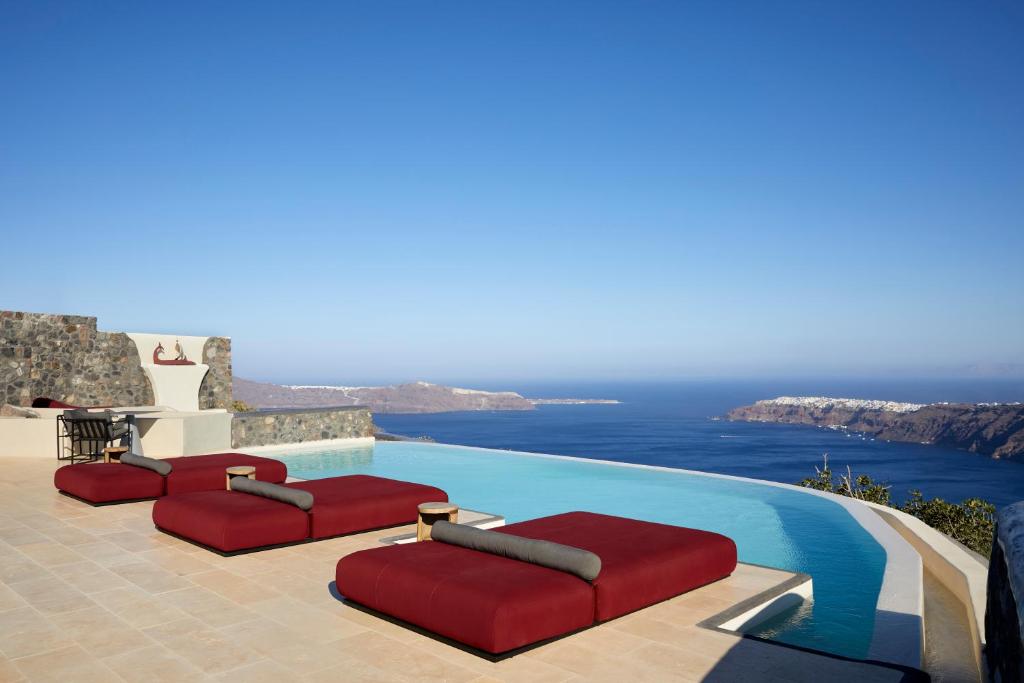 a pool with red cushioned chairs and the ocean at White Pearl Cavalieri in Imerovigli