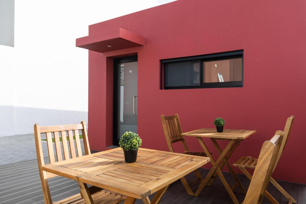 una mesa y sillas en un patio con una pared roja en As Casas da Margarida en Ribeira Grande