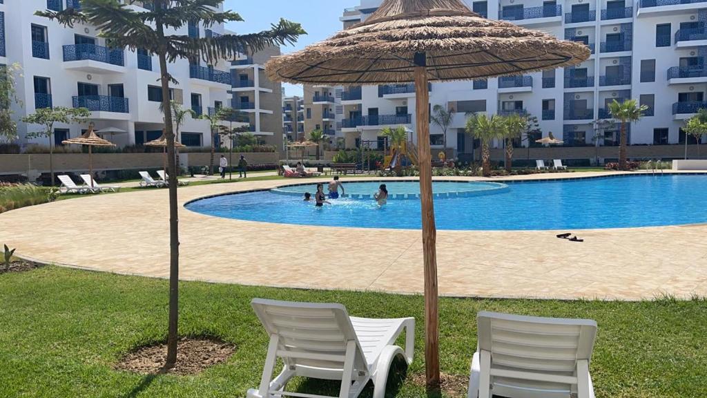 due sedie e un ombrellone accanto alla piscina di Appartement de luxe avec piscine a 5 min de la plage a Martil