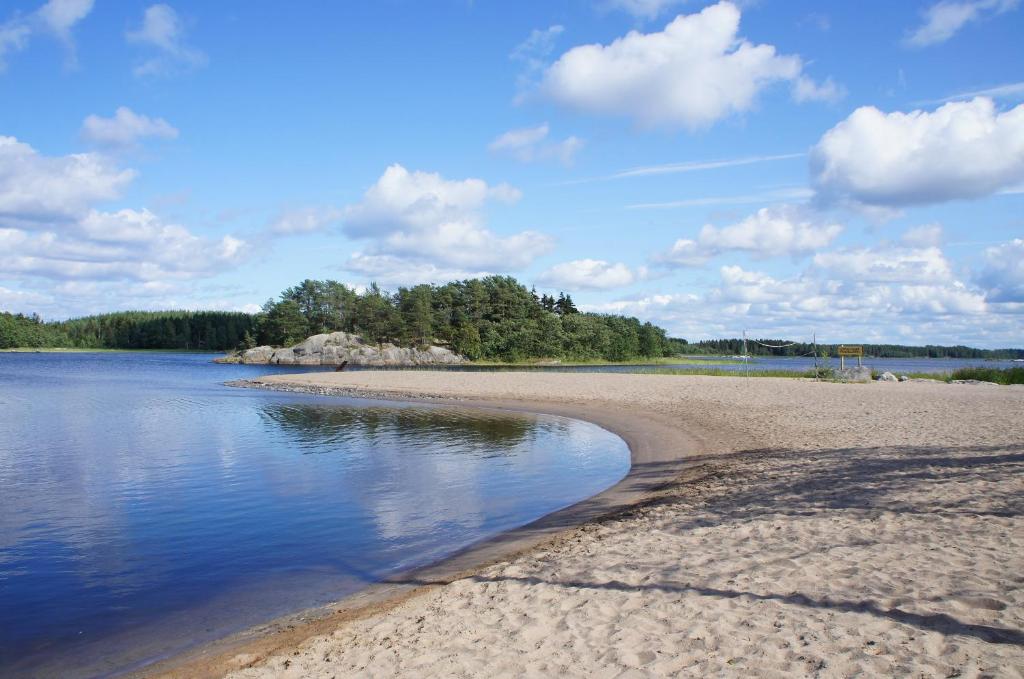 uma praia arenosa com água e árvores ao fundo em Wästinn em Vöyri