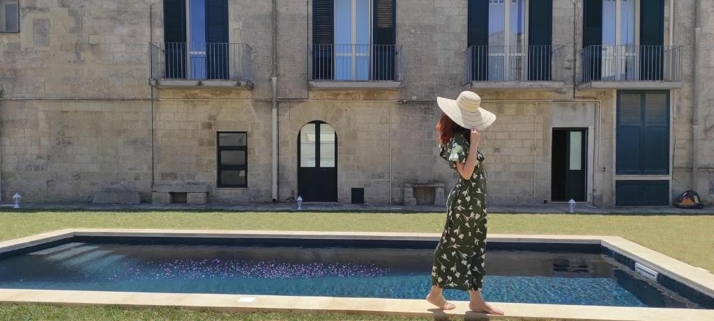 una mujer con un sombrero parada frente a una piscina en Dimora Duchessina Suites de Charme, en Minervino di Lecce