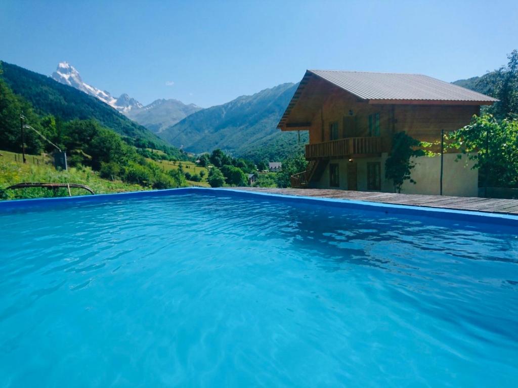 a swimming pool with a house and mountains in the background at Guesthouse Dolra Svaneti in Becho