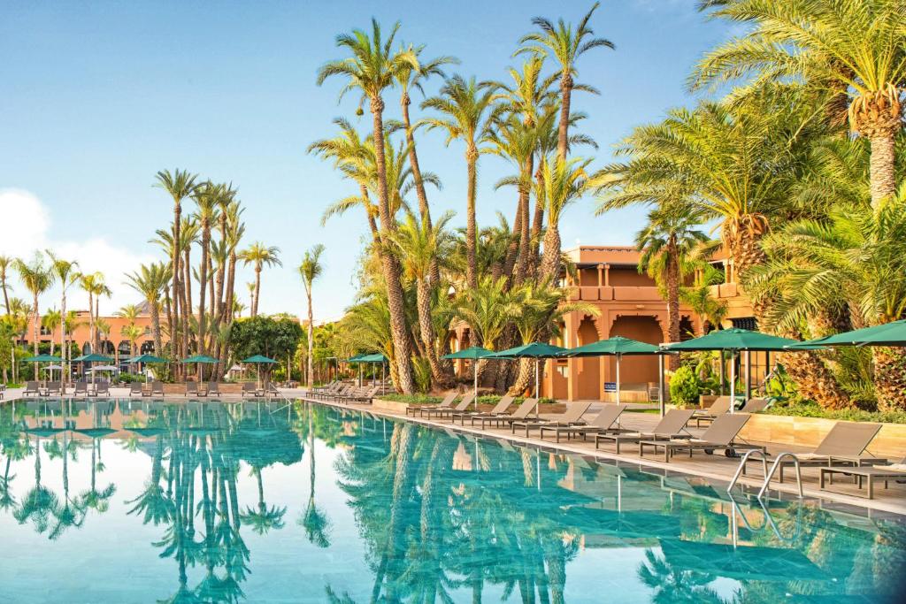 een zwembad met stoelen, parasols en palmbomen bij Hotel Riu Tikida Garden - All Inclusive Adults Only in Marrakesh