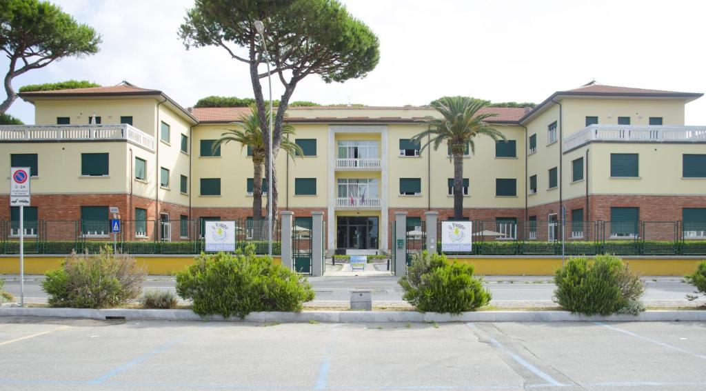 un grand bâtiment jaune avec des palmiers dans un parking dans l'établissement Casa per ferie Il Pioppo, à Marina di Massa