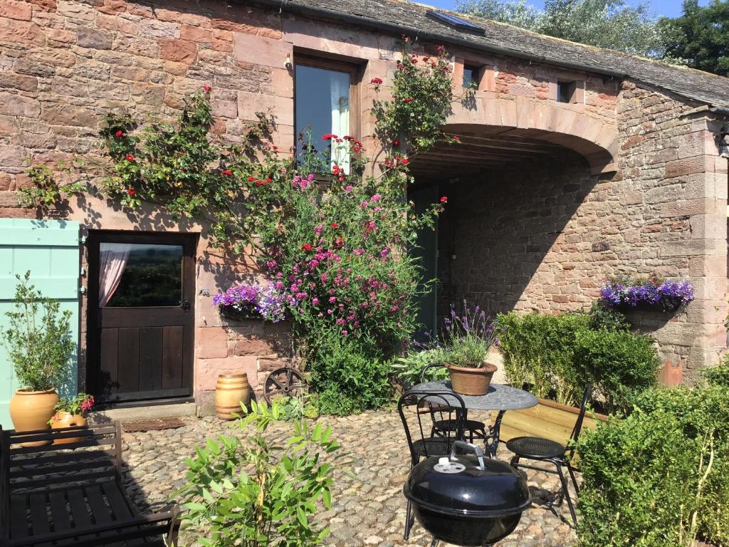 un patio con mesa y sillas frente a un edificio en Historic converted byre in courtyard of 16C house, en Caldbeck