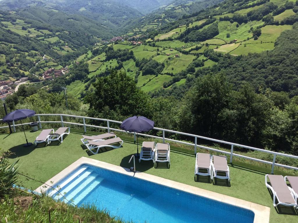 a swimming pool with chairs and umbrellas next to a mountain at LA ALDEA SOÑADA in Oviedo