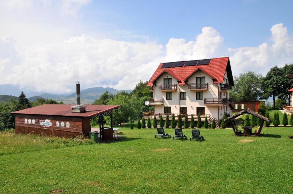 a large house with a red roof with chairs in a field at Pensiunea Recanto in Fundata