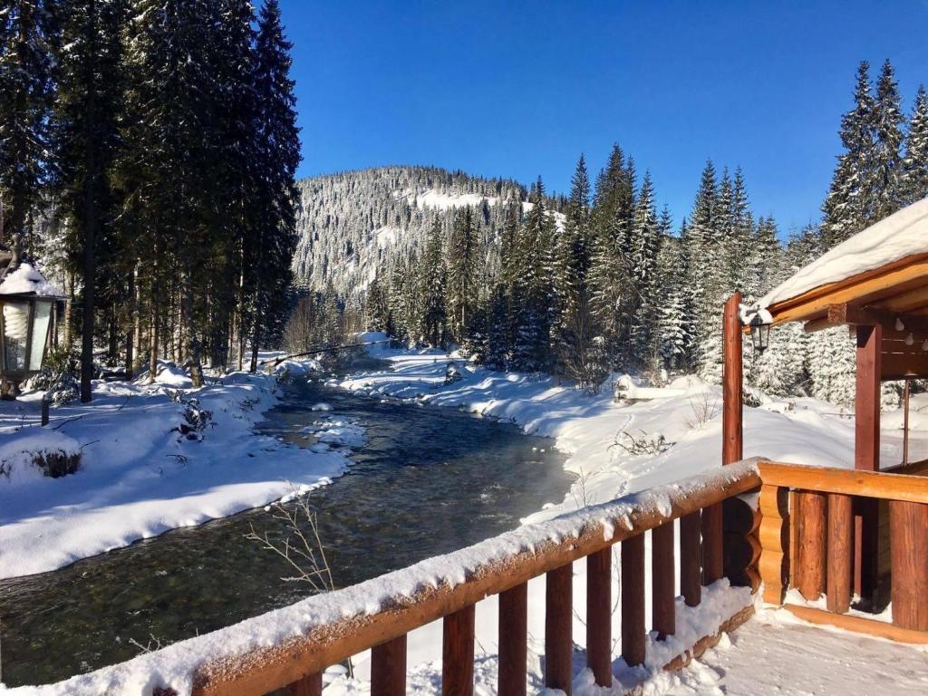 a river in the snow next to a wooden fence at Pensiunea Vanatorul in Obarsia-Lotrului