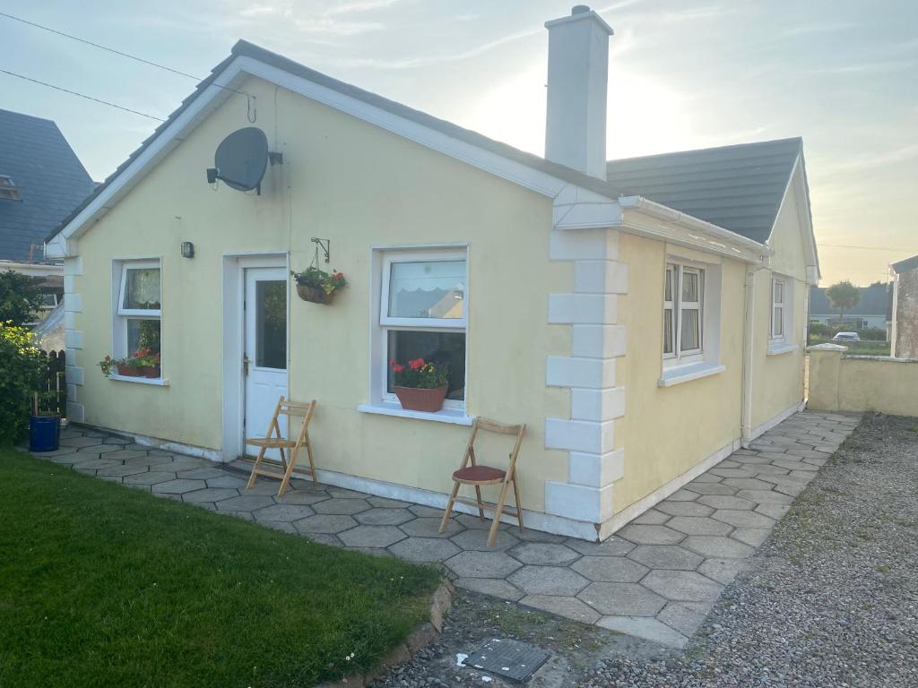 una pequeña casa con dos sillas delante en Primrose Cottage en Gweedore