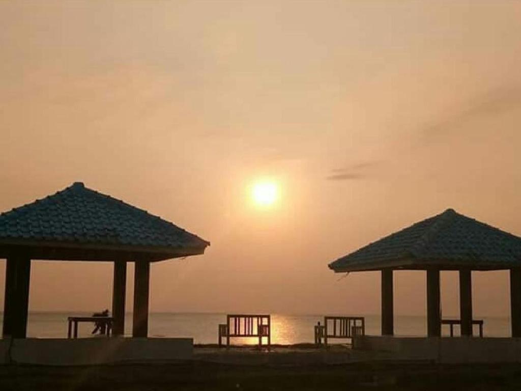 a group of umbrellas on a beach with the sunset at penginapan karanglaut santolo in Cilauteureun