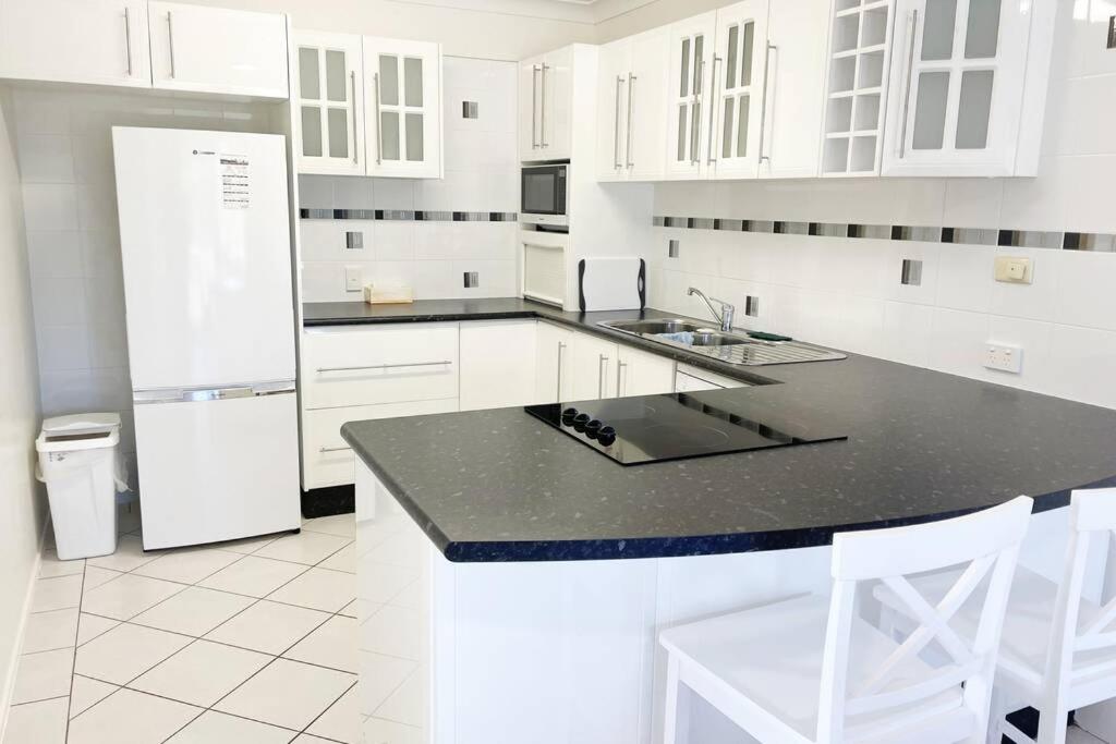cocina blanca con encimera negra y nevera en Crystal Waters-2 bed, 2 bathroom, Beachfront Unit!, en Bongaree