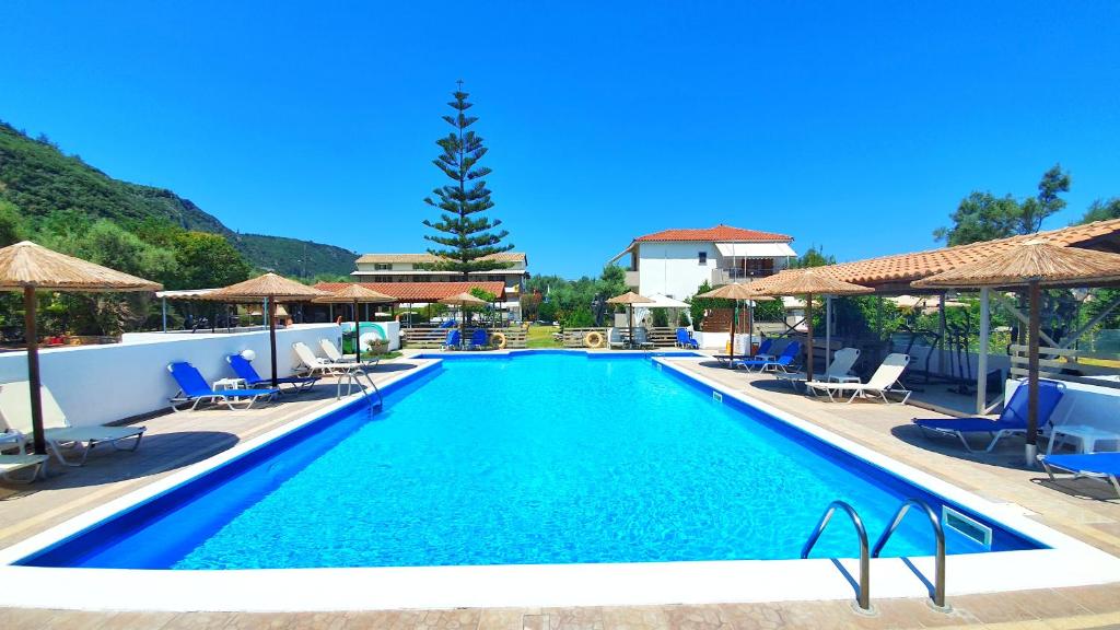 a swimming pool with blue chairs and umbrellas at Alexaria Holidays Apartments in Lefkada