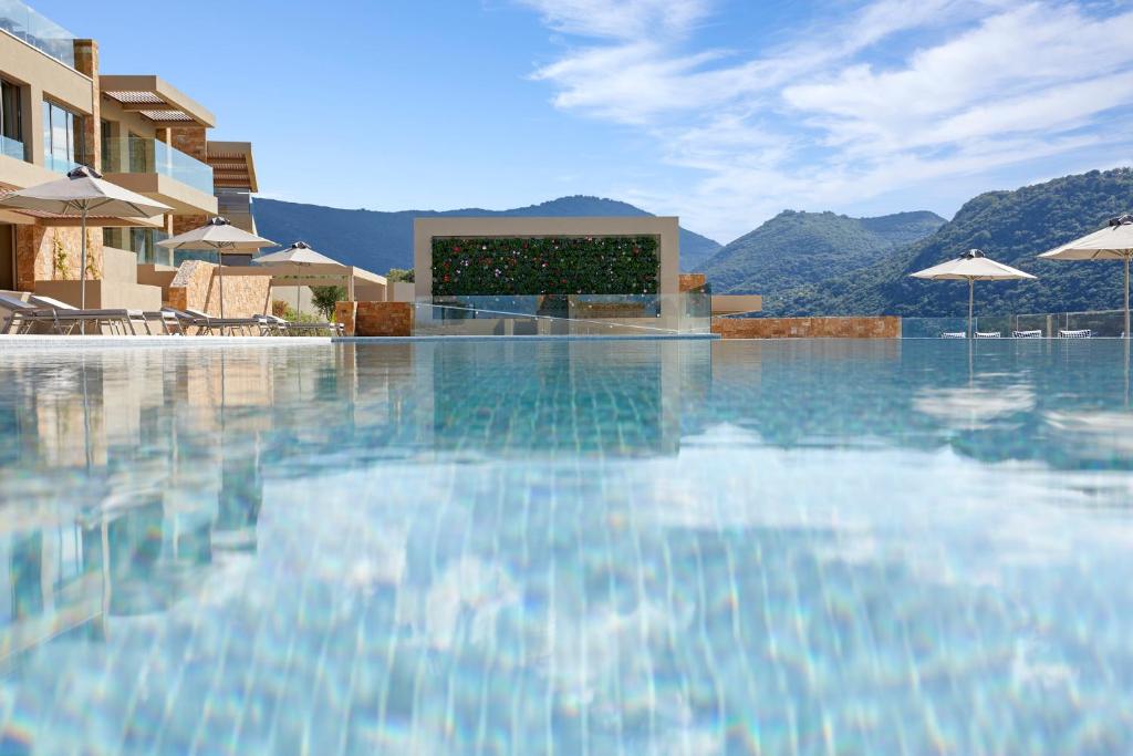 a swimming pool with a building and mountains in the background at Elix, Mar-Bella Collection in Perdika