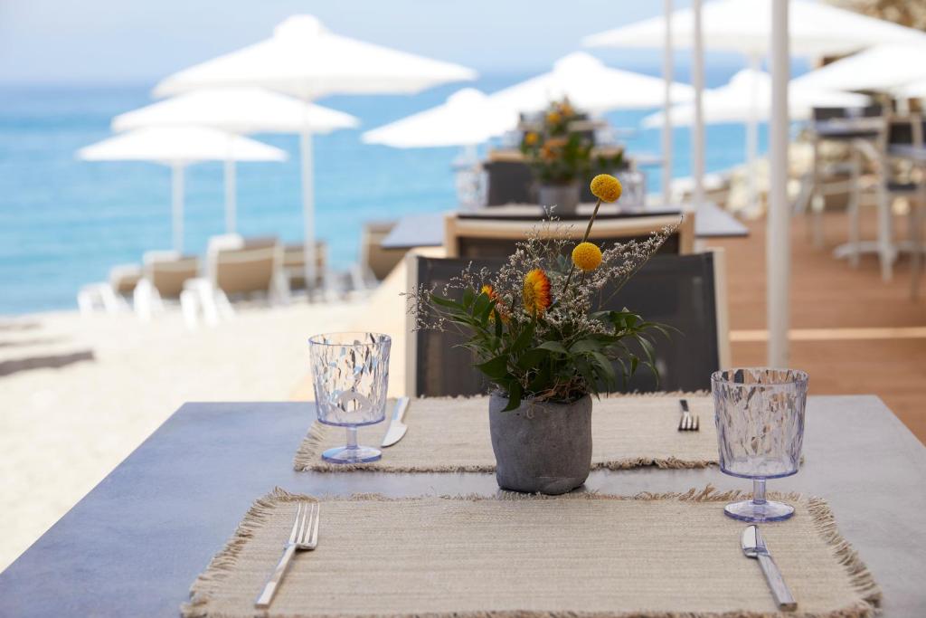 a table with glasses and a vase of flowers on the beach at Elix, Mar-Bella Collection in Perdika