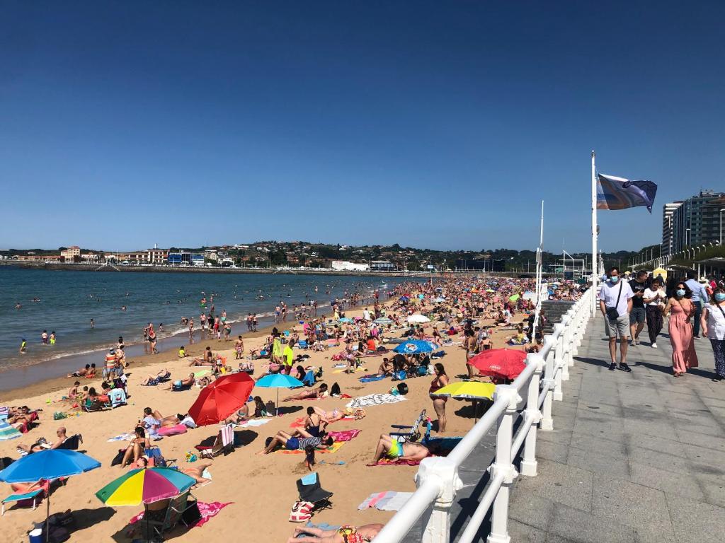 eine Menschenmenge am Strand in der Nähe eines Piers in der Unterkunft Casa en la playa in Gijón