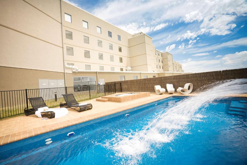 a swimming pool with chairs and a fountain in front of a building at Rydges Mount Panorama Bathurst in Bathurst