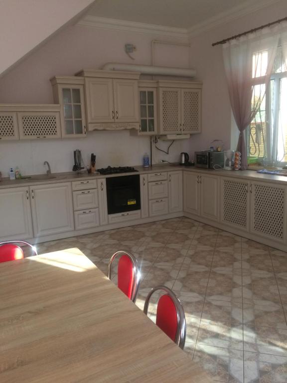 a kitchen with white cabinets and a table with red chairs at Дом на берегу Черного Моря in Zatoka