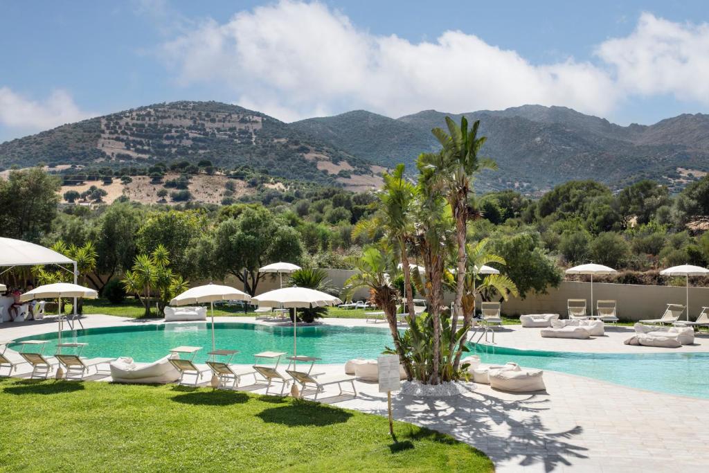 a pool with chairs and umbrellas and mountains in the background at Hotel San Teodoro in San Teodoro