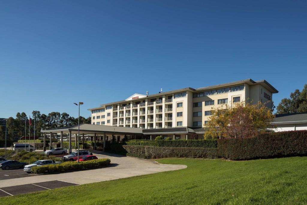 a large building with cars parked in a parking lot at Rydges Norwest Sydney in Baulkham Hills
