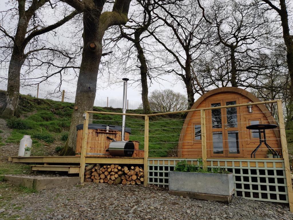 a wooden cabin with a fence and a grill at Tan-y-Dderwen Pod in Machynlleth