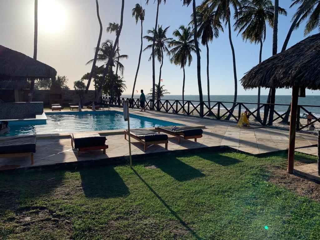 a resort swimming pool with palm trees and the ocean at Condomínio com vista para o Mar e Piscina no CUMBUCO- AP 106 in Caucaia