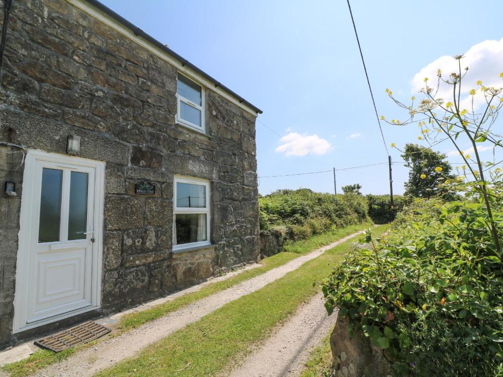 a stone cottage with a white door and a dirt road at Blackberry Cottage in Carbis Bay