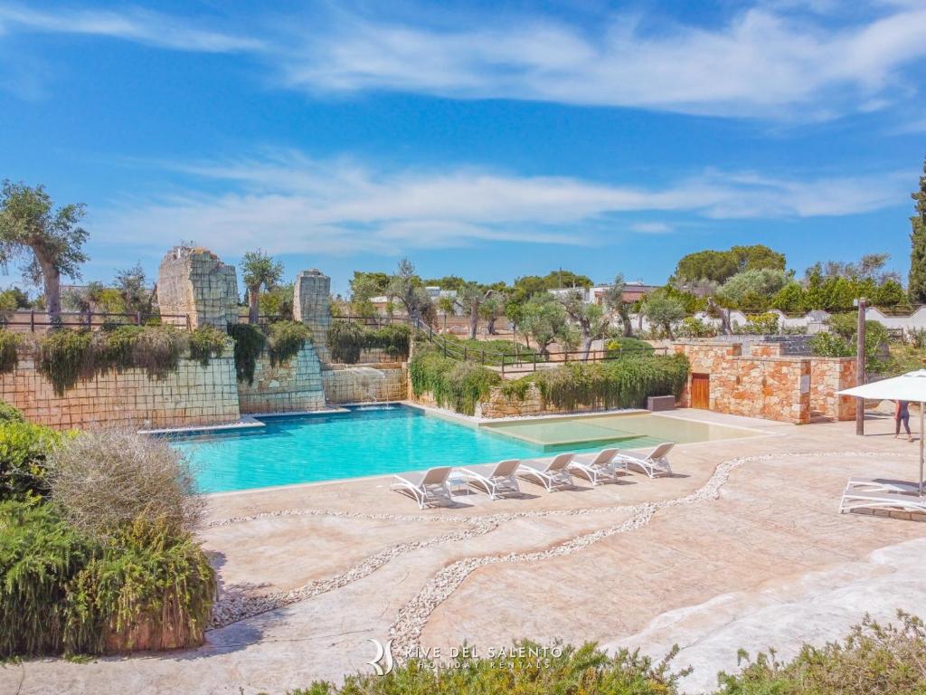 a swimming pool with lounge chairs and a brick wall at Cava Li Santi Residence in Santa Caterina di Nardò