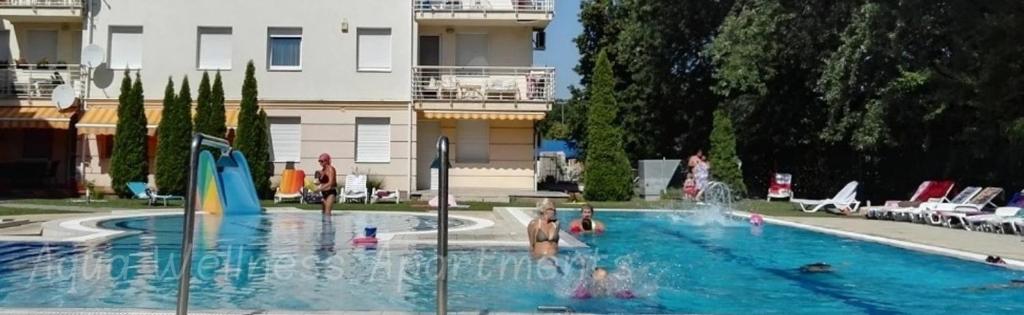 a swimming pool with people playing in the water at Aqua Wellness Apartments in Hajdúszoboszló