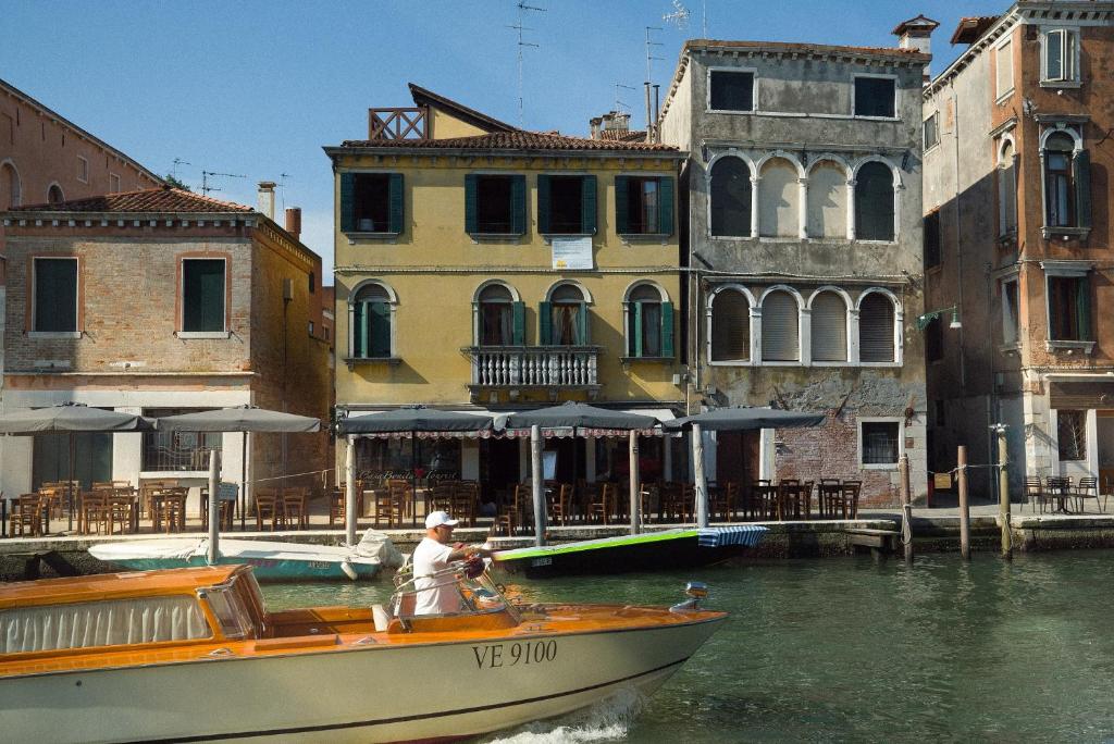 een man in een boot in het water bij gebouwen bij Casa Virginia direct at the canal Cannaregio with own roof terrace in Venetië
