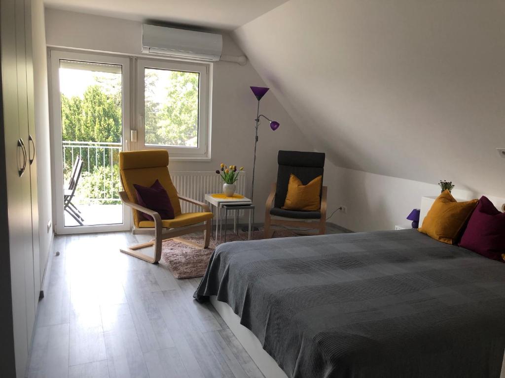 a bedroom with a bed and two chairs and a balcony at Dominik Apartmanház in Velence