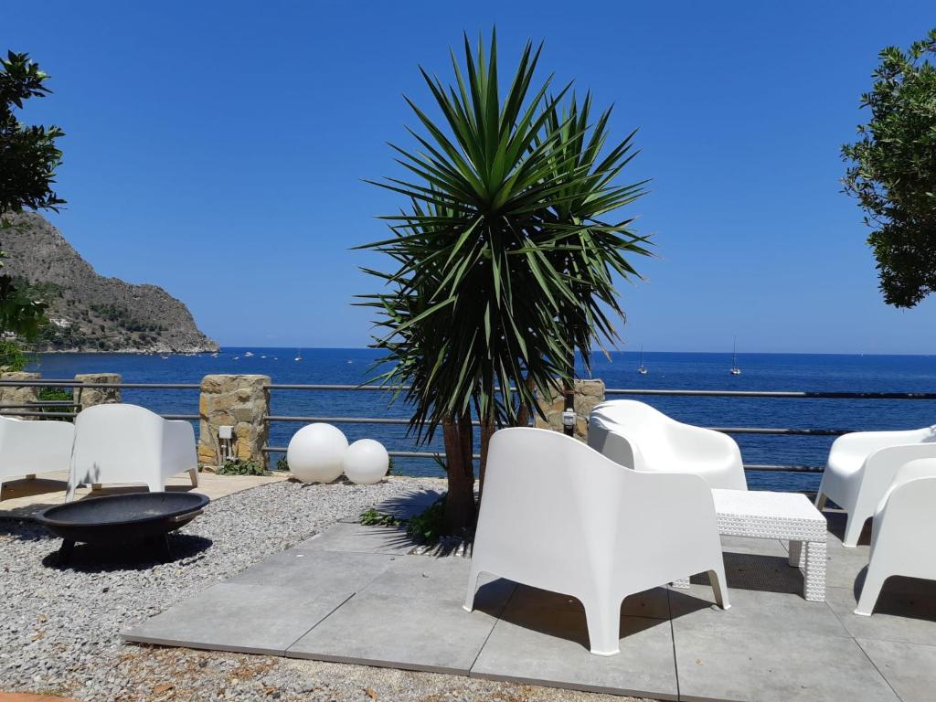 a group of white chairs and a palm tree and the ocean at Capozafferano-Casa Carola in Santa Flavia