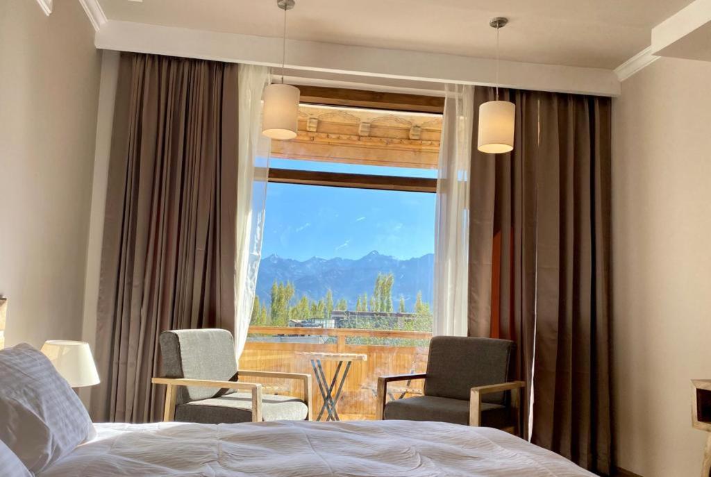a bedroom with a bed and chairs and a window at Hotel Amanthi Ladakh in Leh