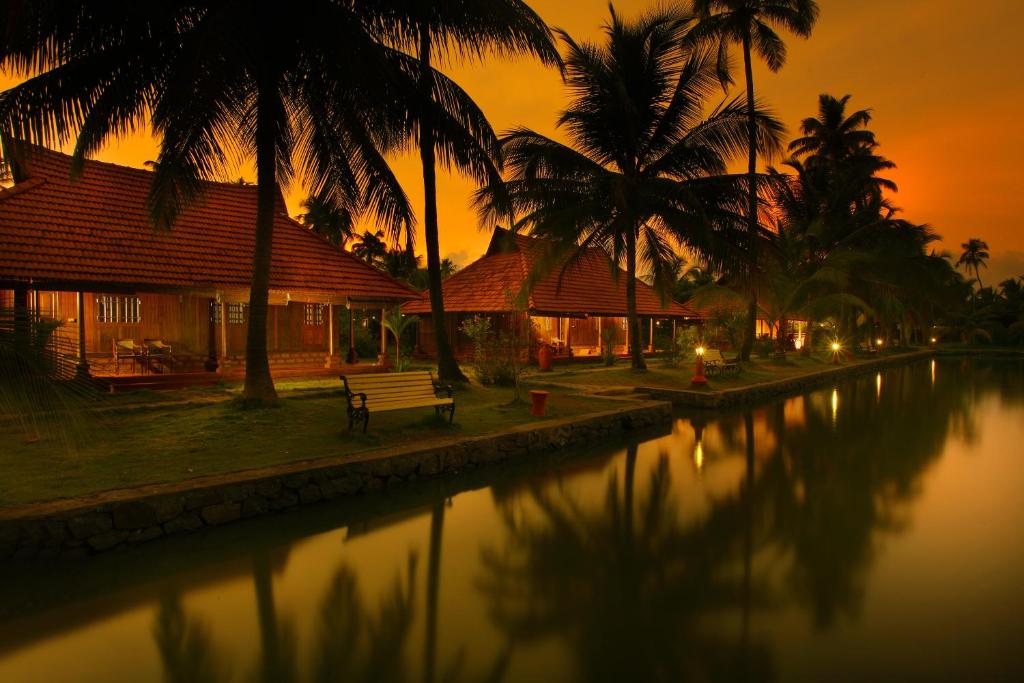 a house with palm trees and a river at sunset at Kondai Lip Backwater Heritage Resort in Cochin