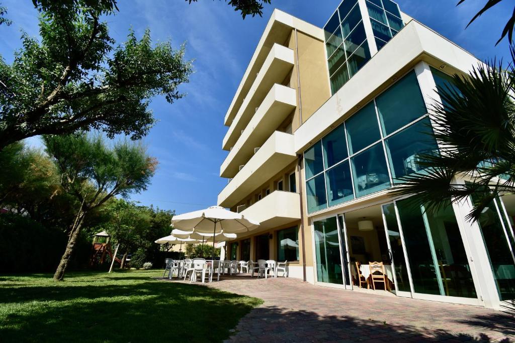 a building with tables and umbrellas in front of it at Hotel Astor in Lido di Classe