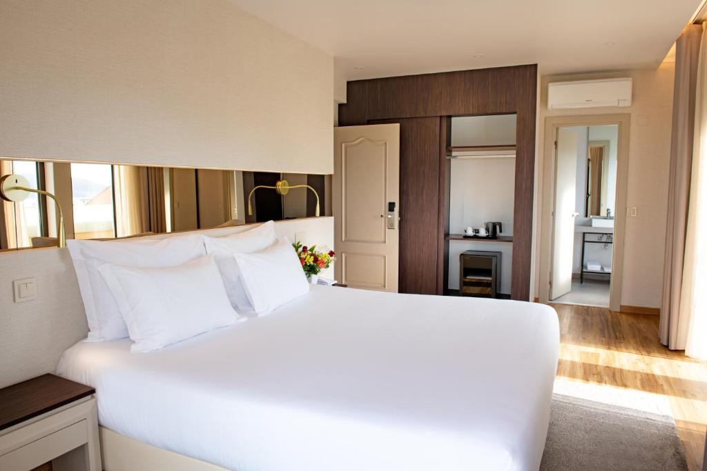 a bedroom with a large white bed and a kitchen at Hotel Cristal Setúbal in Setúbal