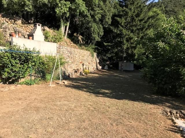 a dirt yard with a stone wall and trees at BEL APPARTEMENT TYPE F3 in Amélie-les-Bains-Palalda