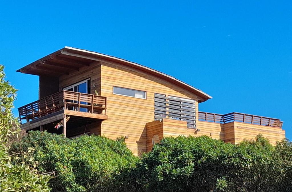une maison en bois avec un balcon au-dessus de quelques buissons dans l'établissement Casa de diseño a pasos de la playa, WIFI banda ancha, teletrabajo, à Los Molles