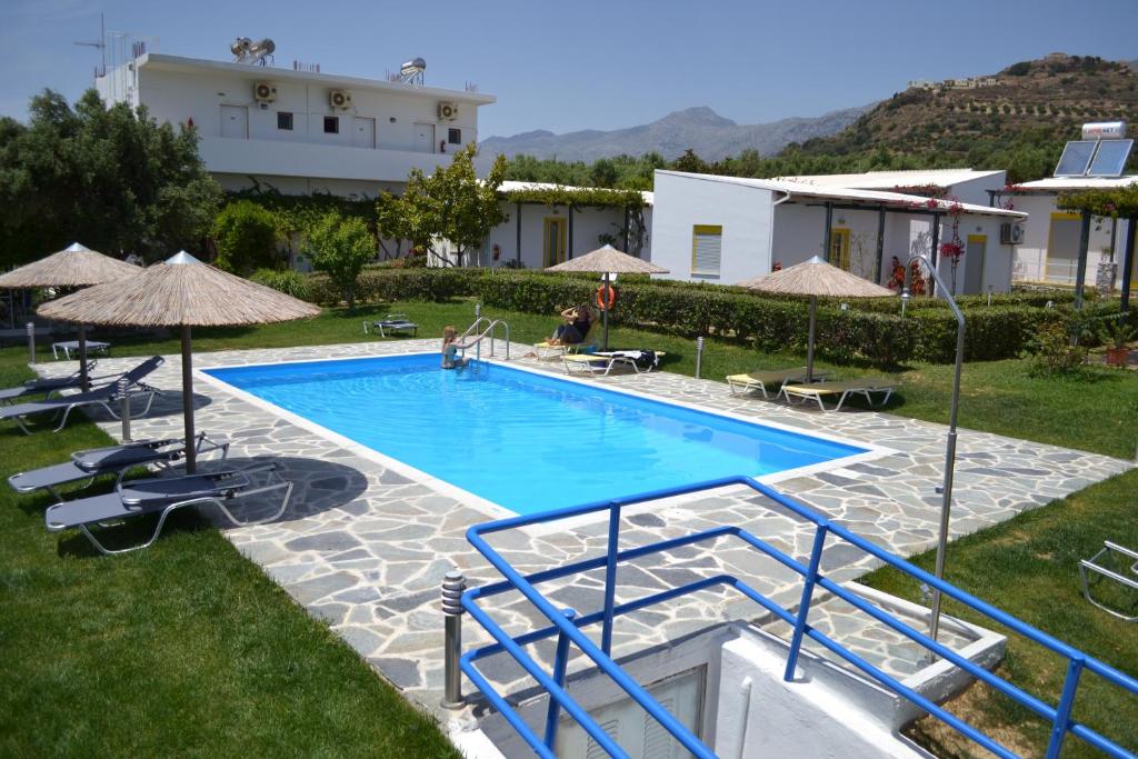 a swimming pool with chairs and umbrellas next to a house at Ikaros Studios in Plakias