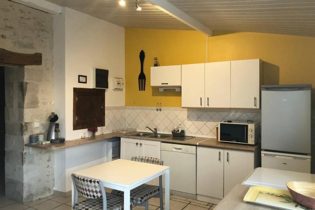 a kitchen with white cabinets and a table and a microwave at Charmante maison dans la vallée de la Charente in Voulême