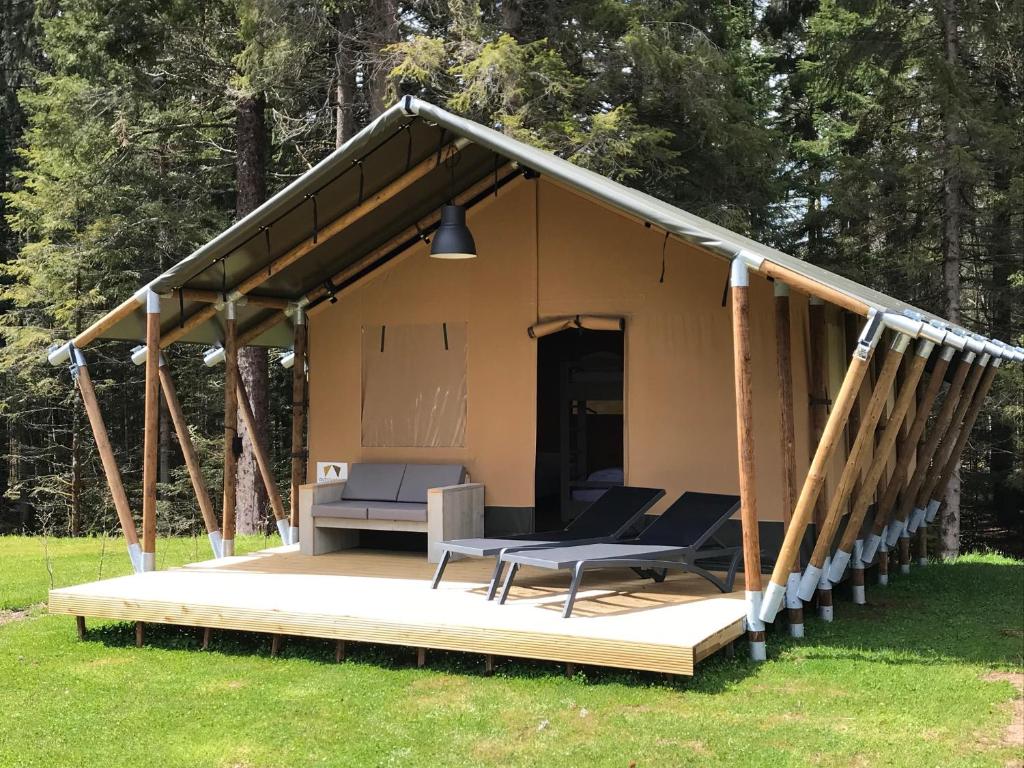 a tent with a porch with a chair and a table at Budget Glamping Safaritent - La Steniole in Barbey-Séroux