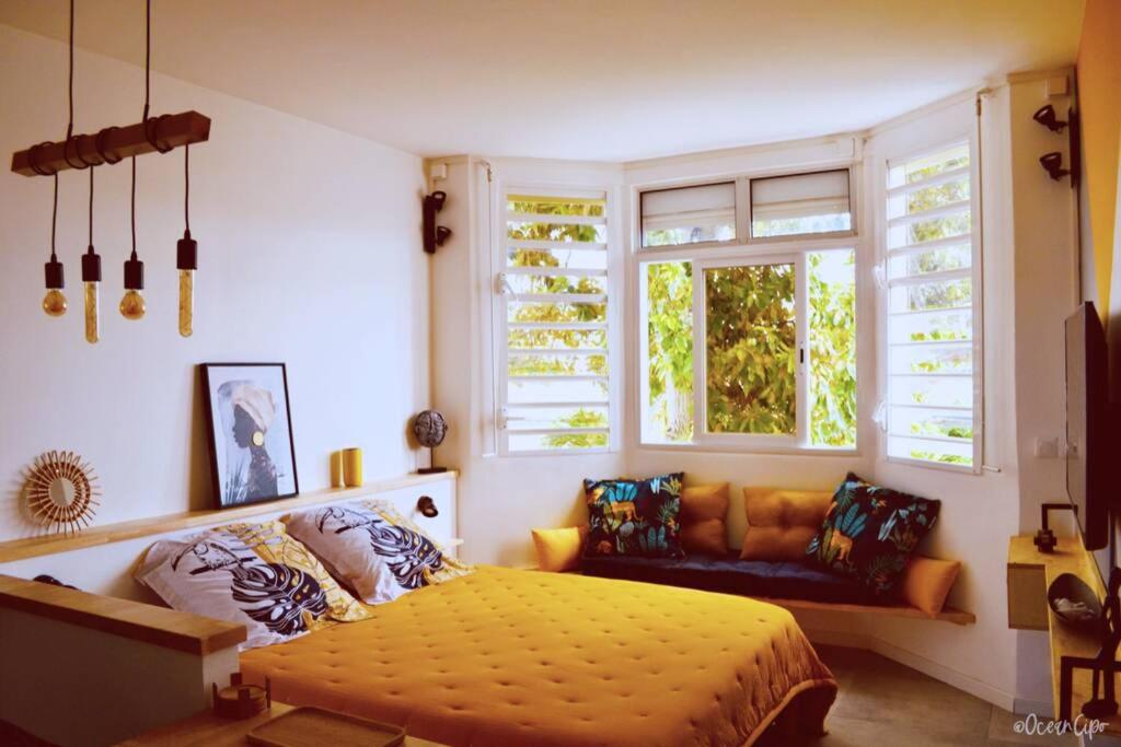 a bedroom with a bed and a couch and windows at Studio Hévéa, expérience de standing à la marina in Saint-François