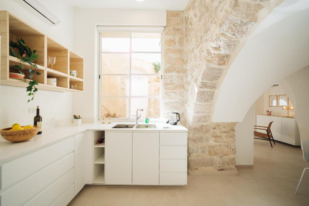a kitchen with white cabinets and a stone wall at חקל תפוחין in Safed