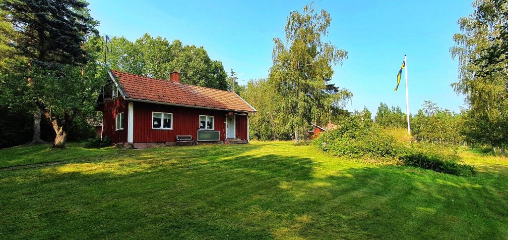 una pequeña casa roja en un patio de césped con una bandera en Lidsbergs torp i Ölme en Kristinehamn