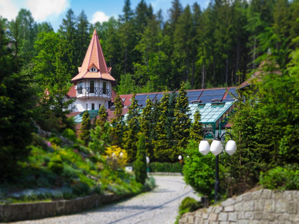 Quaint turreted building peeking through dense evergreen trees along a winding cobblestone path.