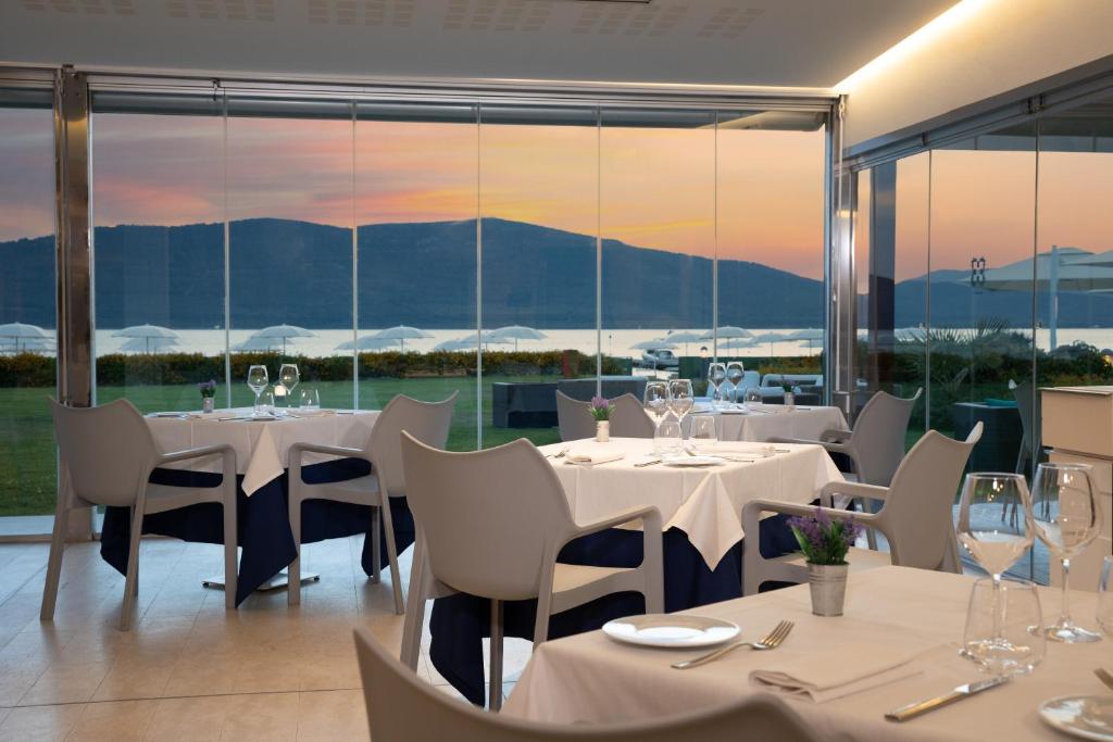 een restaurant met witte tafels, stoelen en ramen bij Hotel Corte Rosada in Porto Conte